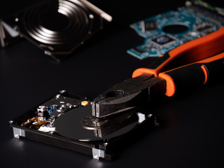 Damaged Hard disk drive and pliers on black background. Open storage device with secret...