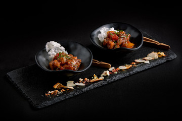 Closeup on tasty stew with vegetables: potatoes, carrots, red pepper, sprinkled with parsley, served in black plates with a spoon on a dark table