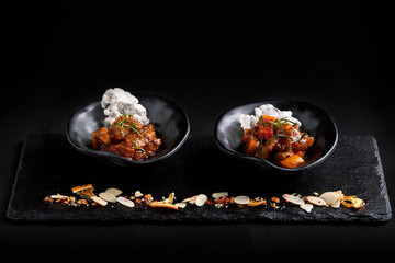Closeup on tasty stew with vegetables: potatoes, carrots, red pepper, sprinkled with parsley, served in black plates with a spoon on a dark table