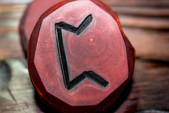Rune Pertho (Peord) red color carved from wood on a wooden background - Elder Futhark