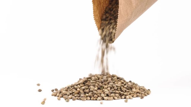 Close-up of hemp or cannabis seeds spilling out of brown eco paper pack. Natural painkiller concept. Isolated, on white background