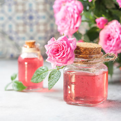 Natural pure rose oil or scented water in bottles for spa, skin care or aromatherapy. Glass bottle on a wooden table, small pink roses with leaves. Organic cosmetics concept.