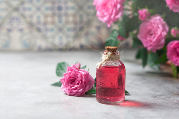 Natural pure rose oil or scented water in bottles for spa, skin care or aromatherapy. Glass bottle on a wooden table, small pink roses with leaves. Organic cosmetics concept.