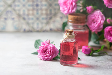 Natural pure rose oil or scented water in bottles for spa, skin care or aromatherapy. Glass bottle on a wooden table, small pink roses with leaves. Organic cosmetics concept.