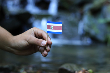 National flag of Costa Rica on wooden stick with water background. Colour man holds state symbol and waves. Concept of humanity and nature. Concept of education and omniscience