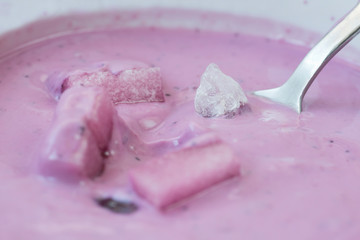 Hidden sugars concept. Fruit yoghurt blueberry in white dish with sinking sugar lumps and one candy on spoon 