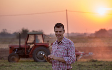 Farmer with tablet in front of tractor