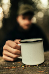 Fototapeta na wymiar Male Hand holding metal cup with hot drink with a person blurred in background.