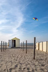 Gardinen Vintage yellow and white beach hut with multi-colored kite in the sky © Erik_AJV