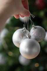 New Year's toys balls of silver color in a female hand on a background of the Christmas tree. Christmas and new year concept.