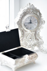 An open vintage box for women's jewelry stands on a white window, near an old watch.