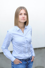 Blonde bussiness woman dressed casual with a perfect smile, standing near a white wall