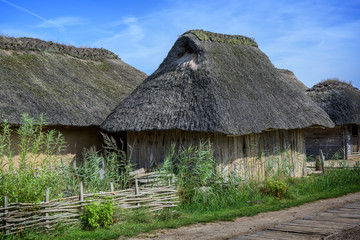 Plakat Historical wooden house with thatched roof in the reconstructed Viking village Haithabu on the banks of the inlet Schlei of the Baltic Sea in Northern Germany, blue sky, copy space