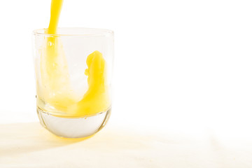 Fresh squeezed orange juice splashes into a glass tumbler.