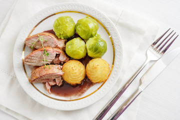 Seared duck breast fillet with duchess potatoes and brussels sprout, a festive dinner on a white table, high angle view from above, selected focus, narrow depth of field