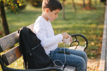 Teenage boy in white shirt use powerbank for charging his smartphone otside. Low battery on smartphone