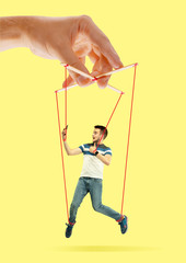 Man like a puppet in somebodies hands on yellow background. Concept of unfair manipulation,...