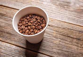 Coffee grains in a paper cup on a wooden background.