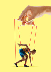 Man like a puppet in somebodies hands on yellow background. Concept of unfair manipulation,...