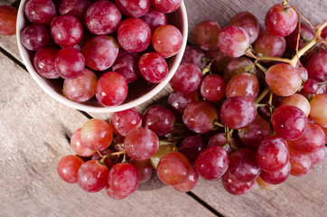 Close Up Ripe red grape bunch on a old wooden surface. Dark moody photo of Pink Grapes in a bowl.