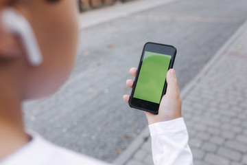 Mock up of teenage boy with wireless headphones use phone otside. Green screen