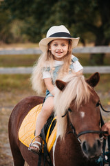 Adorable little girl riding a pony at summer