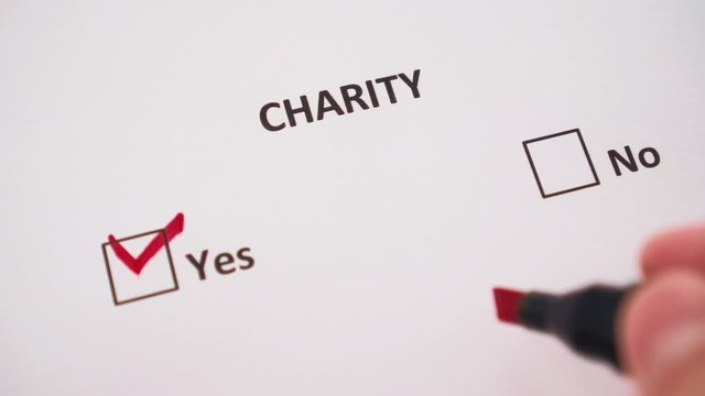 The hand ticks the word YES under the word CHARITY with a red marker on the white page of the questionnaire. The concept of financial donations and generosity