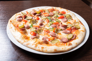 Cheap pizza with sausages, cucumbers, cherry tomatoes, and herbs.