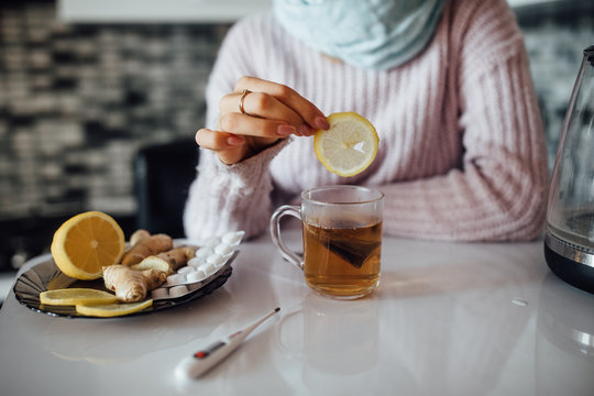 Close up ptoto, sick woman hands at kitchen putting lemon  at cup with tea. Illnes concept.