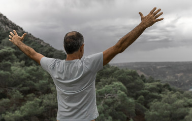 Fototapeta na wymiar An elderly man standing on top of a mountain with his arms outstretched. Beautiful view of the mountains and sky from the back of a man