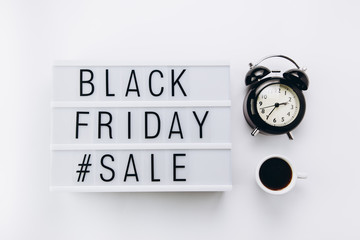 Creative Top view flat lay promotion composition with cup of coffee, alarm clock and Black friday sale text on lightbox white background copy space