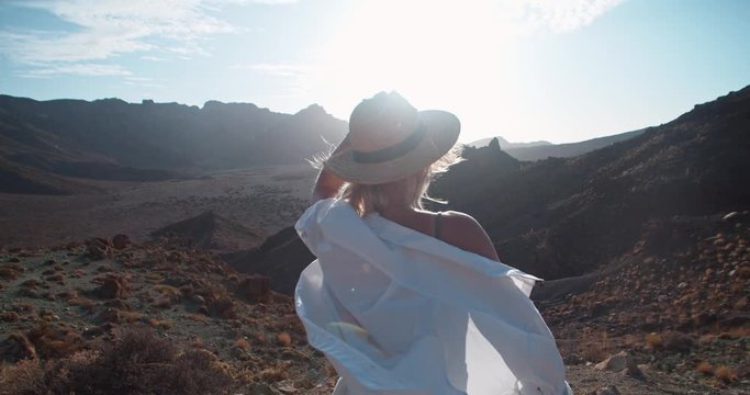 Beautiful woman observing stunning scenic landscape of Teide, Tenerife. Female tourist holding strawhat staying in wind enjoying vacation travel to volcanic desert.
