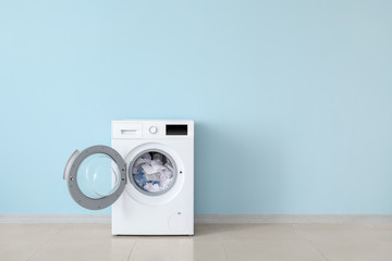 Modern washing machine with laundry near color wall - obrazy, fototapety, plakaty