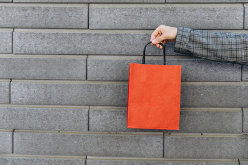 Woman in gray suit holds red paper bag on gray brick wall background