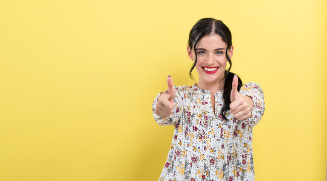 Young woman giving thumbs up on a yellow background