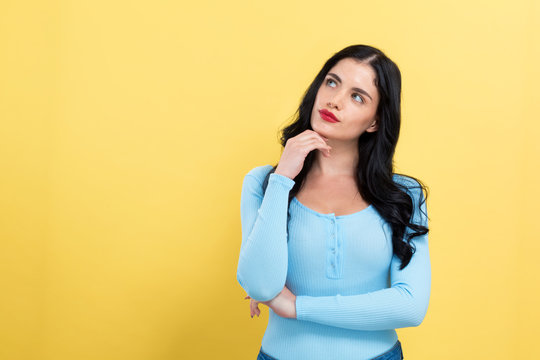 Young woman in a thoughtful pose on a yellow background