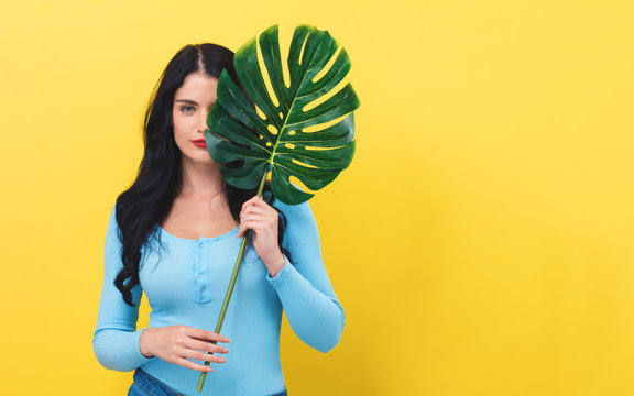 Young woman with a trendy tropical leaf on a yellow background