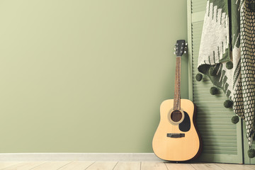Modern acoustic guitar and folding screen near color wall