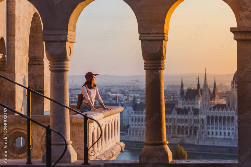 Wall mural A happy young woman enjoying her trip to the Castle of Budapest in Hungary on the view point from Fisherman Bastion on sunrise.