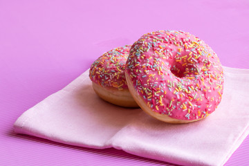 Donuts covered with pink icing and colored pastry topping on a pink background. Copy space.