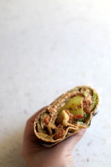 Holding a tortilla wrap with roasted vegetables, guacamole and sauce. Selective focus.
