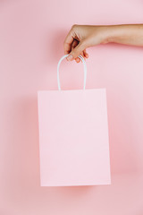 Female hand holding pink paper bag isolated on pink background