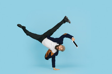 Young caucasian businessman having fun dancing break dance on blue studio background. Management, flexible, freedom, professional occupation, alternative way of modern working. Loves his job