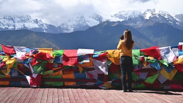 Young woman photographer taking photographs of Meili snow mountain infront tibetan buddhist prayer flags in Yunnan, China