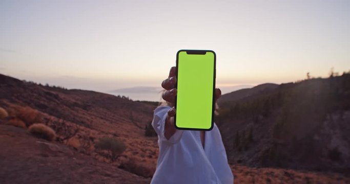 Close-up young woman holding mock-up smartphone greenscreen in beautifful Martian landscape. Tourist girl with mobile phone in the mountains at sunset.