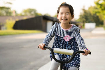 Cute little Asian girl learning ride a bicycle without wearing a helmet