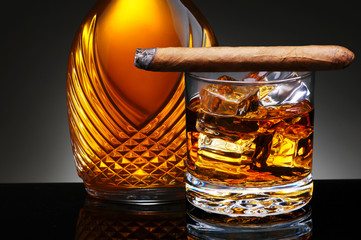 Closeup of an elegant decanter and a glass of scotch on the rocks with a lit cigar laying across...
