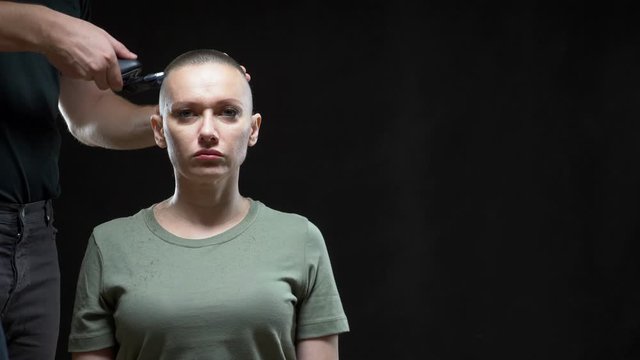 concept military girl. hands of a man hairdresser shave a woman's head bald, army hairstyle. Black background