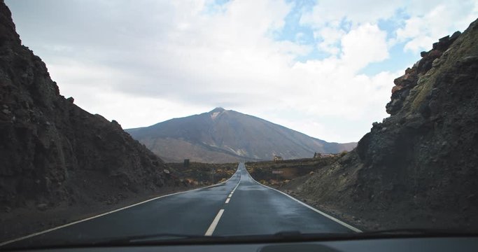 Driving car on highway in wonderful desert countryside. Front-window car view of amazing Teide volcano in martian landscape. Tenerife, Spain.