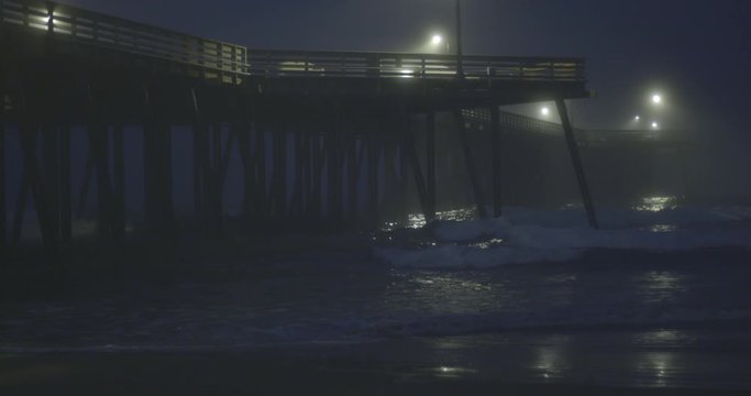 Close view of Pismo Beach Pier at night, with fog rolling in over the Pacific Ocean.
